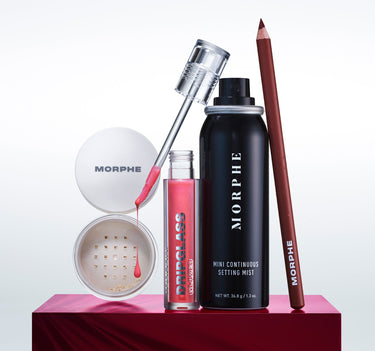 Morphe makeup products including a setting mist, brush, and other items on a red platform with a white background.